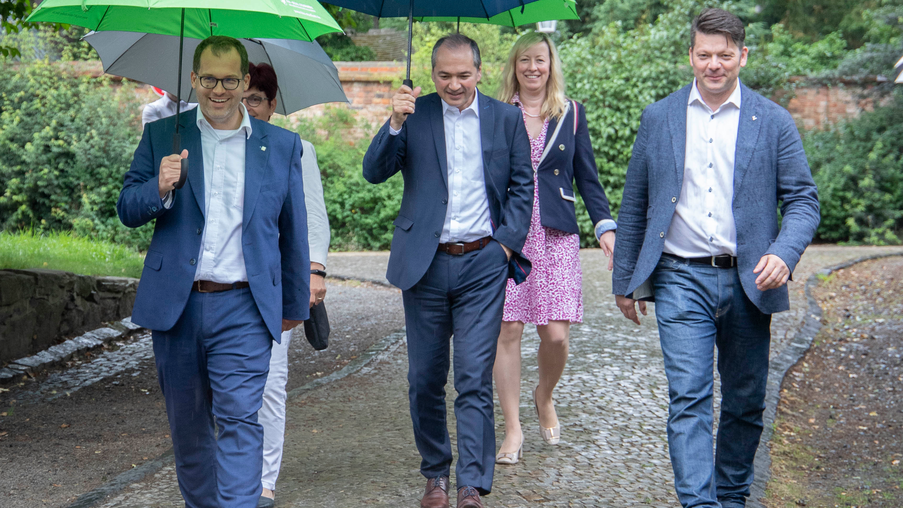 3 Männer und 2 Vrauen mit Regenschirm beim Spaziergang