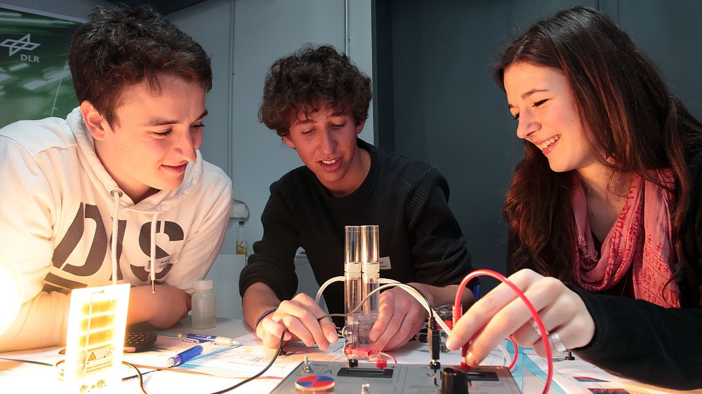 Two male and one female student are sitting at a table and experimenting with a switching device.