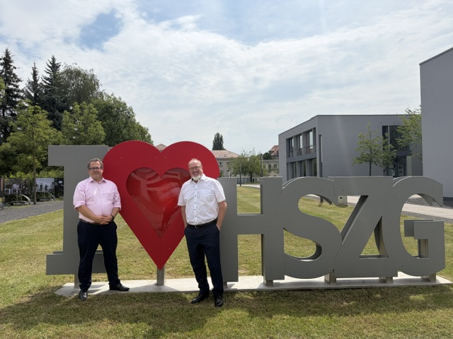: Prof. Dr.-Ing. Alexander Kratzsch and Prof. Dr.-Ing. Sascha Müller-Feuerstein in front of the "I Love HSZG" logo on campus