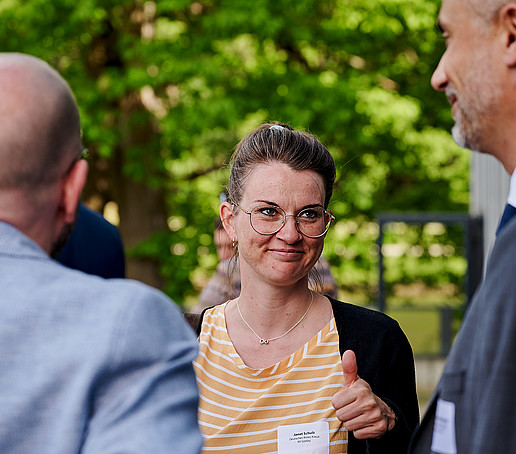 Eine junge Frau hält beim Get Together einen Daumen hoch und lächelt den Dekan an.