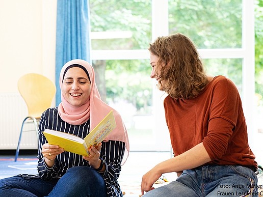Two women are sitting on the floor laughing.