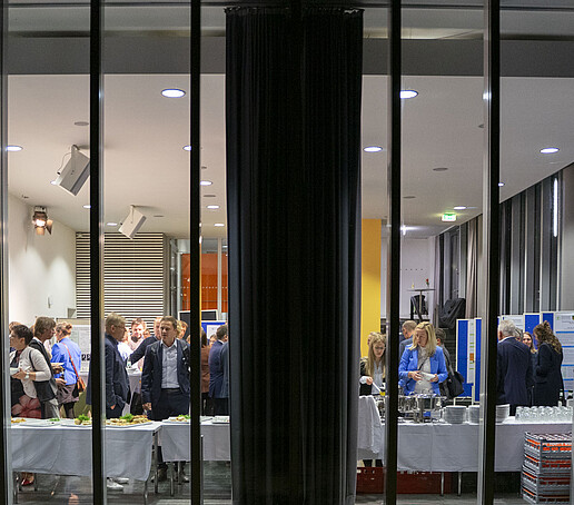 Through the glass pane from outside, you can see the guests in the auditorium as they help themselves to the buffet.