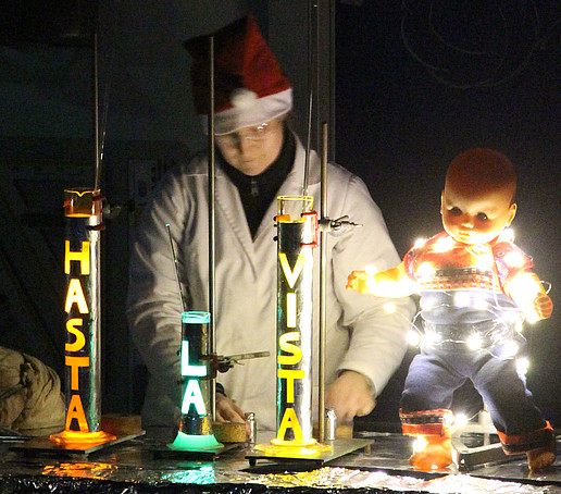 Chemistry employee in a Christmas hat stands at the experiment table. In front of him are three rockets with the inscription: Hasta la vista.