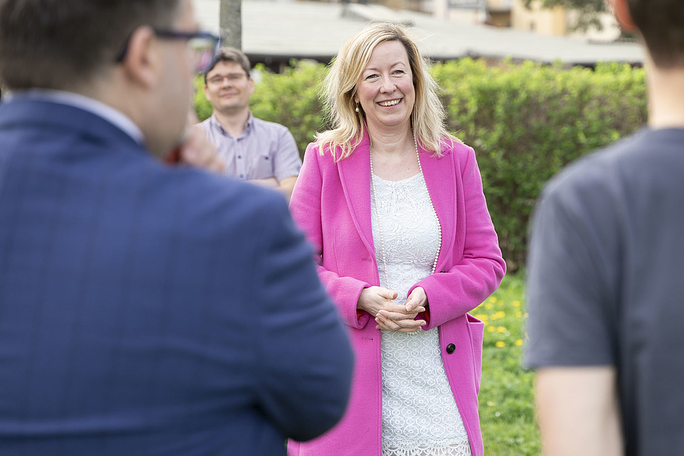 Frau Prof. Dr. Sophia Keil in einer leuchtend pinken Jacke und weißem Kleid lächelt während einer Unterhaltung im Freien.