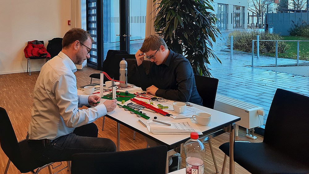 Zwei Workshopteilnehmer sitzen am Tisch und bauen mit Lego-Steinen.