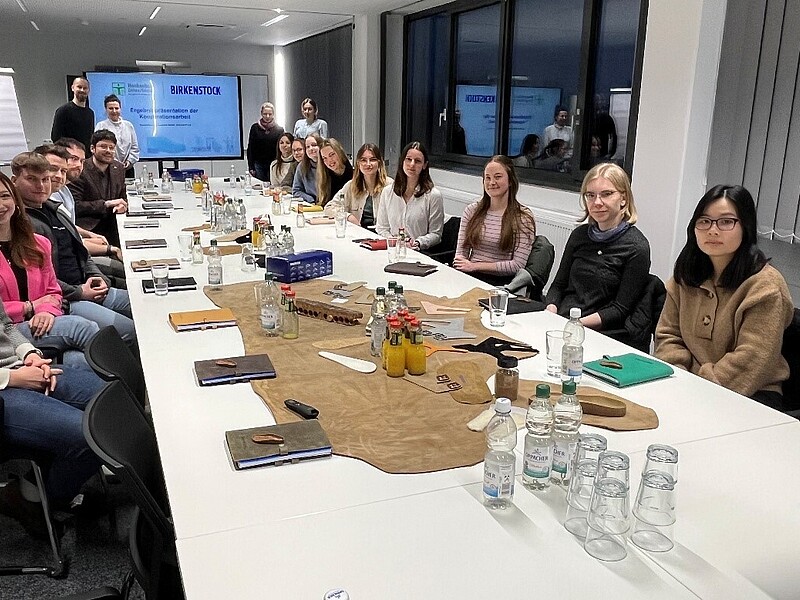 Master's students sit at a long table with a screen at the end.