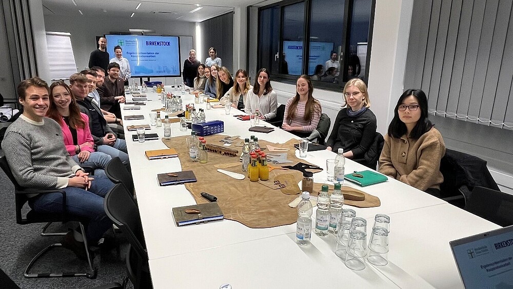 Master's students sit at a long table with a screen at the end.