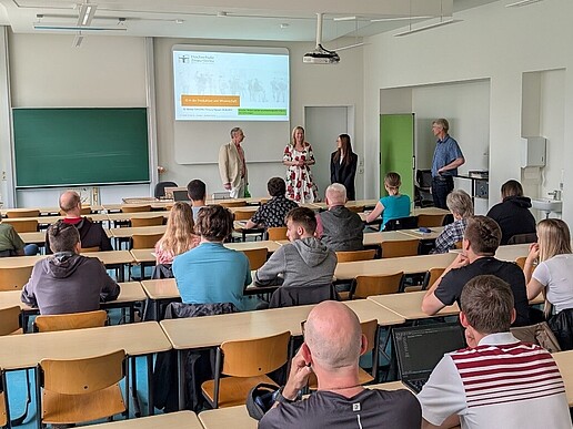 The Vice Rector stands in the seminar room in front of rows of occupied chairs and welcomes the audience.