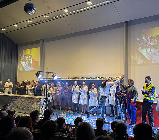 The entire show lecture team stands as a group in a row on the stage and applauds.