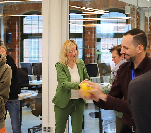 In a large room, workshop participants pass an orange ball to each other.