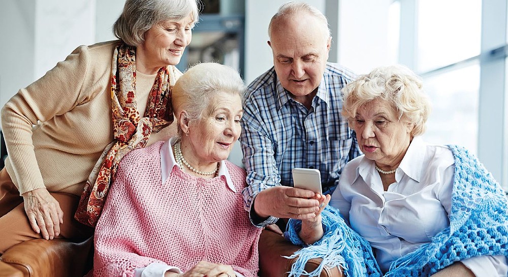 Four senior citizens sit together and look at a cell phone display