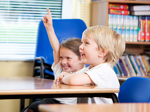 Two primary school children are sitting at the school table. The girl speaks up.