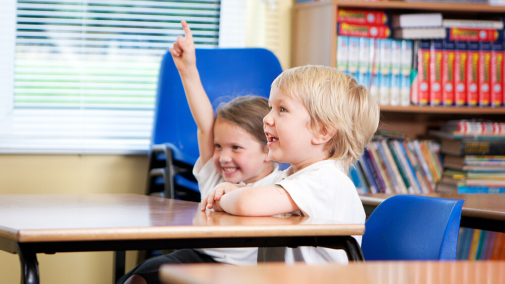 Two primary school children are sitting at the school table. The girl speaks up.
