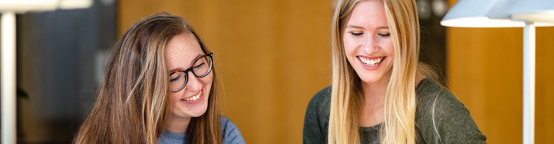 Master of Arts Fachübersetzen Wirtschaft Deutsch/Polnisch - Zwei lachende Studentinnen lesen etwas von einem Zettel ab.
