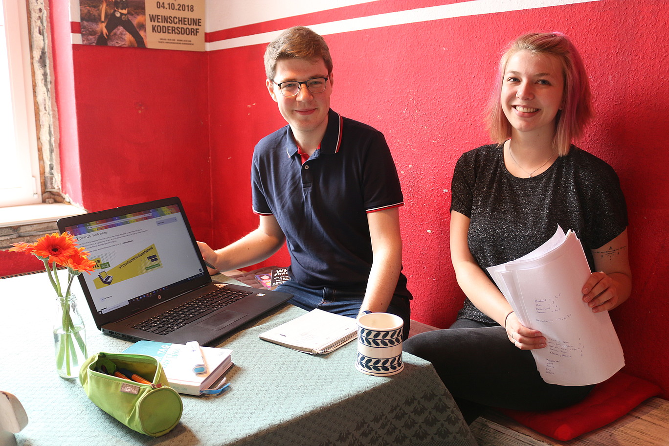 Students Cornelius Baier and Carolin Renner lead through the Virtual University Info Evening. They sit at the table and laugh.