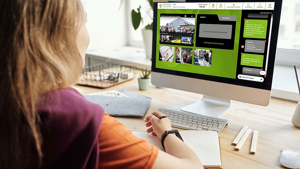A young woman sits at her desk. The online platform for the HSZG's university information day is displayed on the PC screen in front of her.