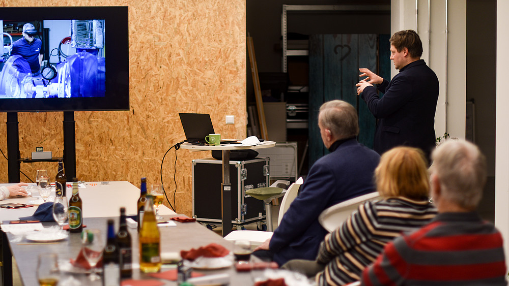 An employee stands in front of a screen in a lecture hall. Audience members are sitting at the table.