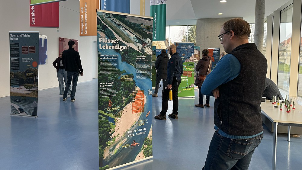 A visitor stands in front of a roll-up in the foyer of Haus Z Vier, surrounded by other visitors to the exhibition.
