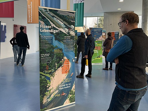 A visitor stands in front of a roll-up in the foyer of Haus Z Vier, surrounded by other visitors to the exhibition.
