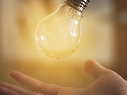 A light bulb hovers above an open hand. It is brightly lit from behind.