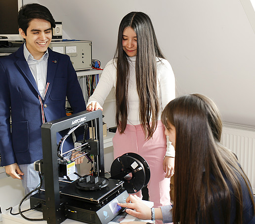 Three Mexican students stand around their self-developed robot and talk.