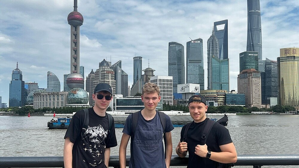 Three students stand on a viewing platform in front of the Shanghai skyline.