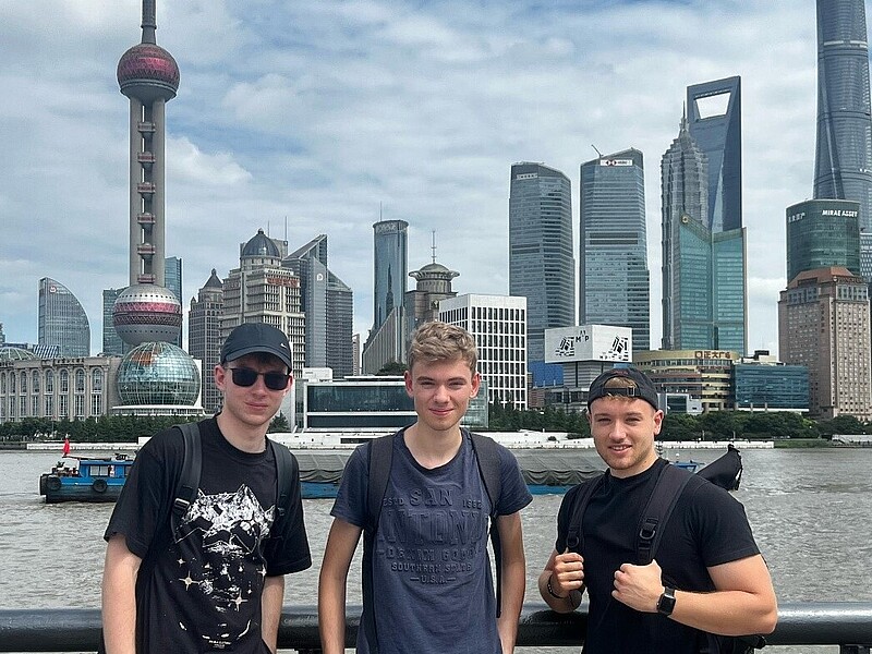 Three students stand on a viewing platform in front of the Shanghai skyline.