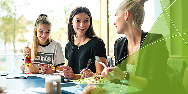 Drei junge Frauen sitzen in der Mensa und essen.