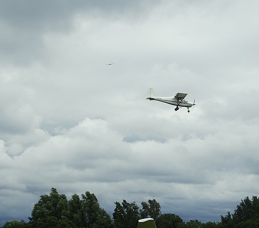 Ein Ultraleichtflugzeug ganz klein im bewölkten Himmel.