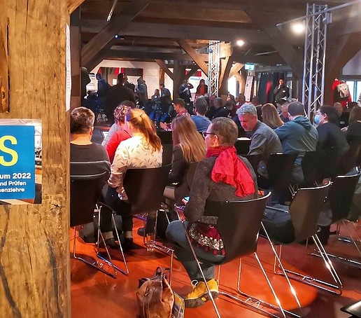 In the event hall, rows of chairs are full of people looking ahead.
