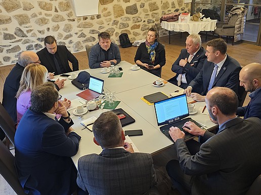 Many representatives of cities and educational institutions sit around a table and talk.