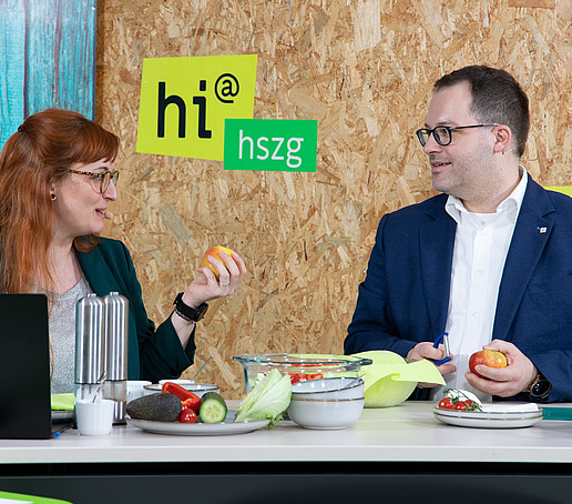 Victoria Hohlfeld and the principal are standing at the table with salad ingredients in front of them. They are smiling and chatting.