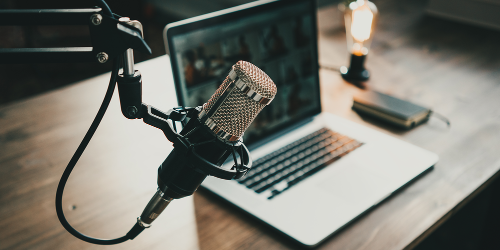 A laptop stands on a wooden table, a professional microphone hangs in the foreground.
