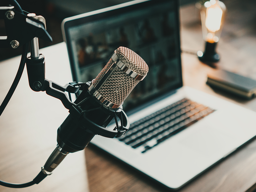 A laptop stands on a wooden table, a professional microphone hangs in the foreground.