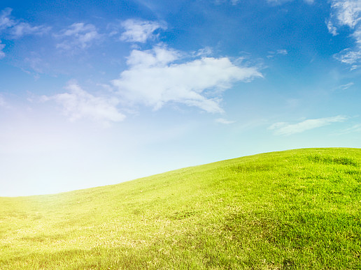 a green meadow merges into a grassy hill, above it a blue sky with scattered clouds