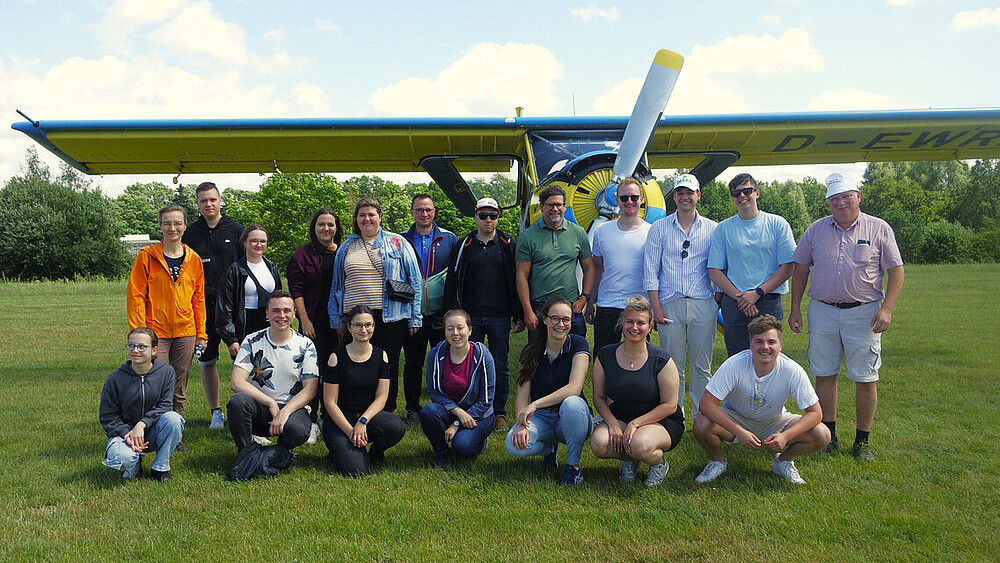 Gruppenbild: Studierende und Professoren stehen und hocken vor einem gelb-blauen Flugzeug.
