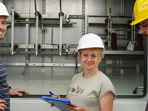 Three researchers are standing in front of an open container at the DC-LabSaxony construction site in Zittau. The research infrastructure for direct current grids is being built there.