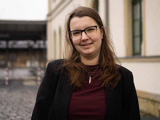 Riccarda Svarovsky vor einem Bahnhofsgebäude lächelt in die Kamera.