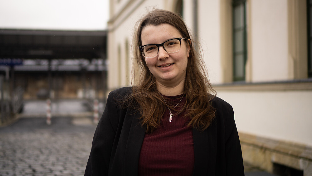 Riccarda Svarovsky vor einem Bahnhofsgebäude lächelt in die Kamera.