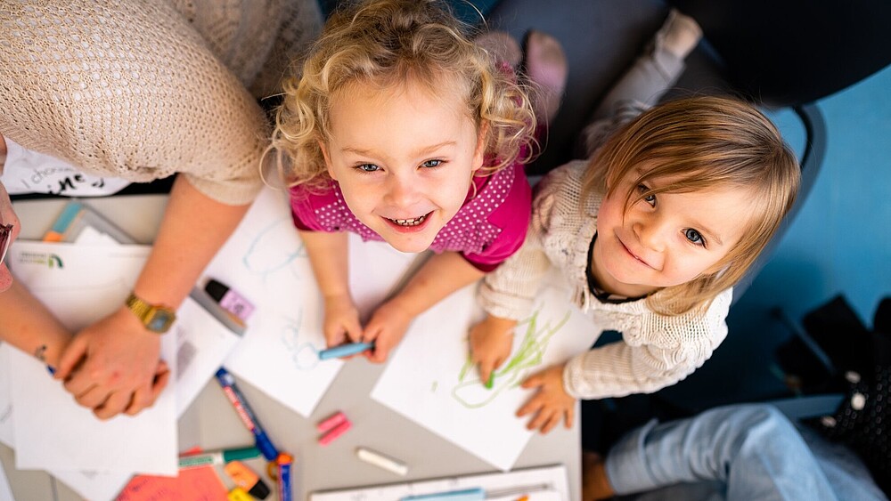 Zwei Kindergartenkinder lachen in die Kamera.