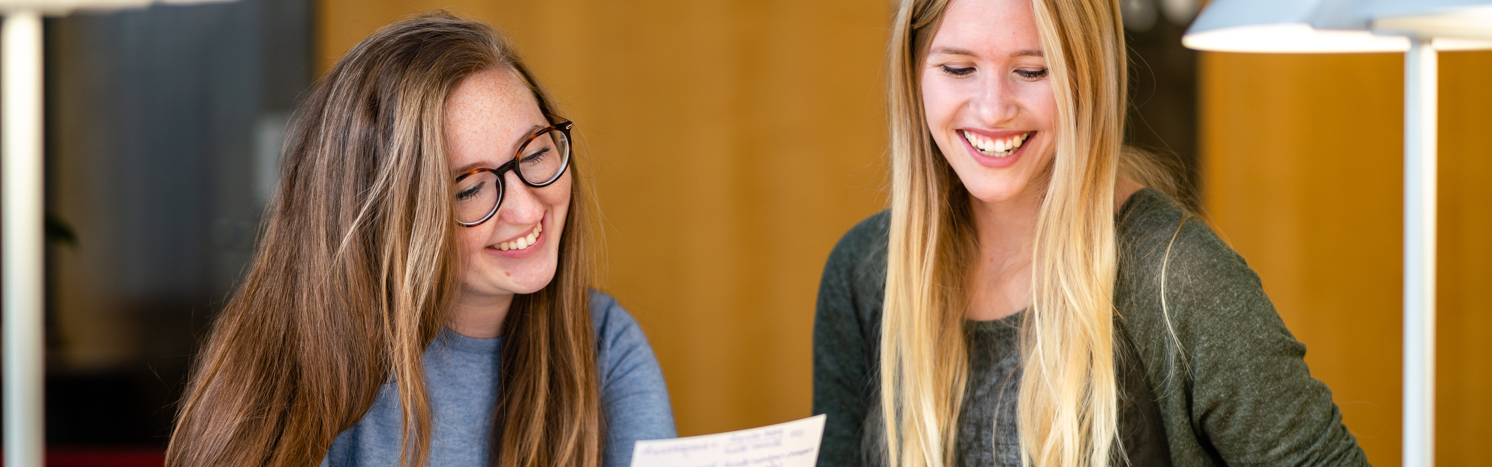 Master of Arts Fachübersetzen Wirtschaft Deutsch/Polnisch - Zwei lachende Studentinnen lesen etwas von einem Zettel ab.