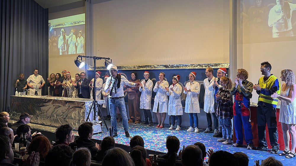 The show lecture team stands in a row on the lecture hall podium and applauds.