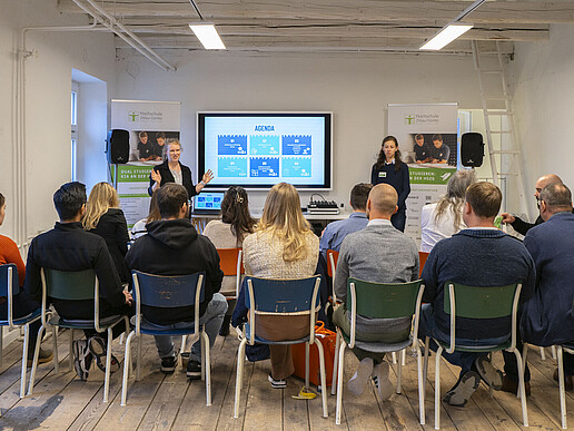 Workshop participants sit on rows of chairs and listen to two moderators.