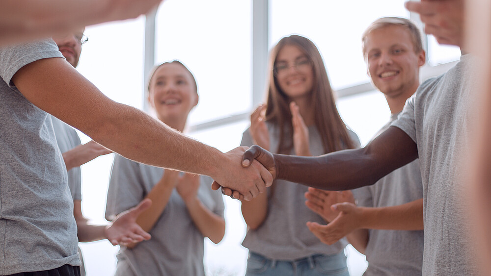 Junge Menschen stehen im Kreis und reichen sich die Hand.