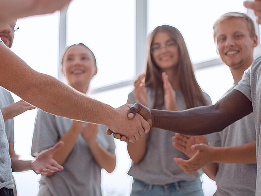 Junge Menschen stehen im Kreis und reichen sich die Hand.