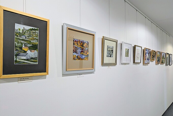 Multicolored paintings hang side by side on a white wall.