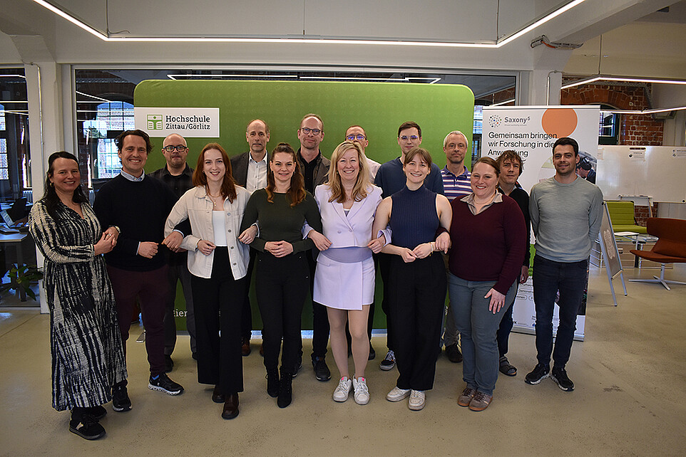 Group photo of the participants in front of a green press wall.