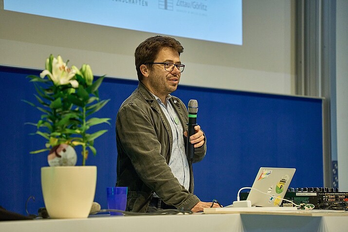 Prof. Weber, microphone in hand, stands in front of a lectern in the lecture hall and gives a speech.