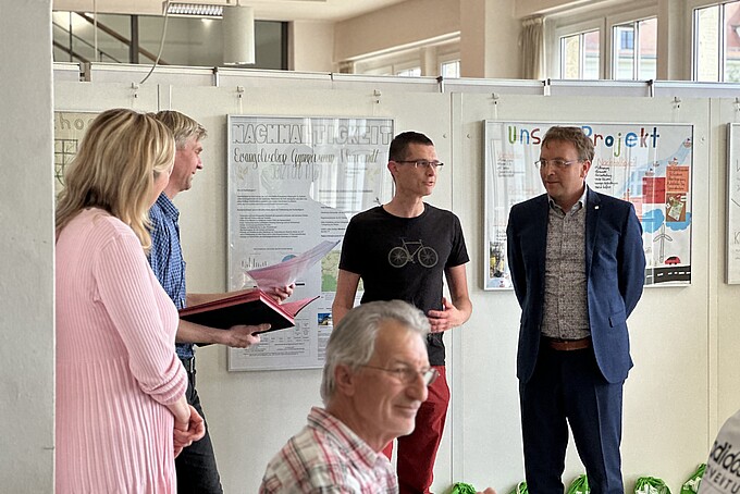 The Vice-Rector, the Dean and a student in front of a poster wall on the topic of sustainability