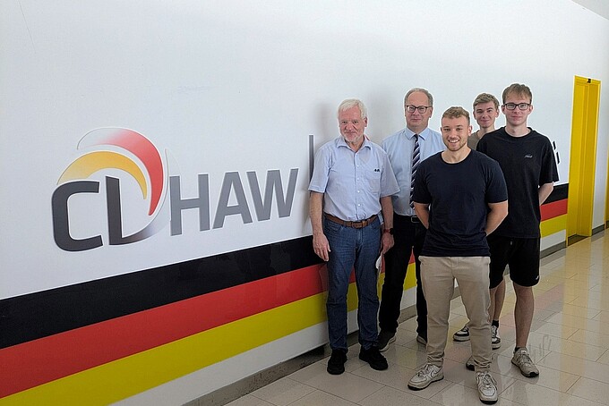 Two professors and three students stand in a corridor next to the CDHAW lettering.